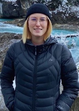 Alyssa wearing a black coat and standing in front of a river